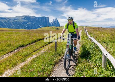 cyclist with an electric mountain bike (e-bike) pedaling in Alpe di Siusi, Seiseralm, South Tyrol, Dolomites, Italy Stock Photo