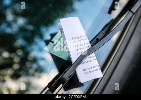 Essen, North Rhine-Westphalia, Germany - A parking ticket is stuck on the windshield wiper on the windscreen of a car in a parking lot. Stock Photo