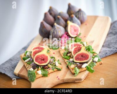 Homemade tasty colorful open sandwiches with slices of fig and pieces of cheese on crisp rye bread among aromatic green leaves of rocket salad and pink flowers Stock Photo