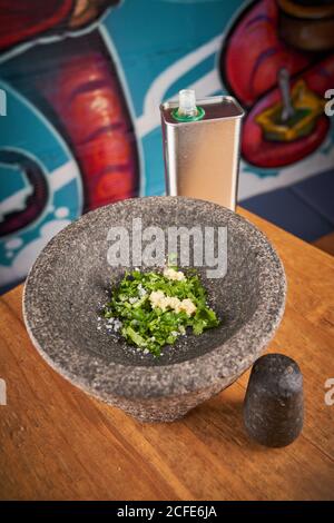 Closeup of gray massive mortar filled with chopped greens and minced garlic with salt placed on table Stock Photo