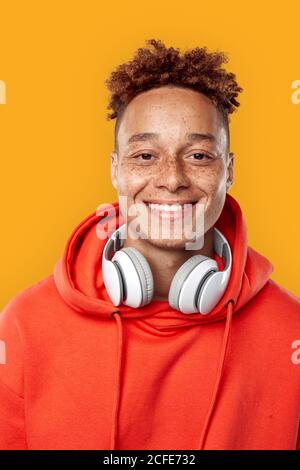 Freestyle. Mulatto freckled guy in hoodie and headphones standing isolated on yellow smiling cheerful close-up Stock Photo