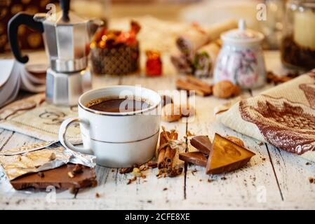 Coffee mug, chocolate, coffee beans, cinnamon sticks and spices on white wooden table. Good morning breakfast or coffee break set background. Stock Photo
