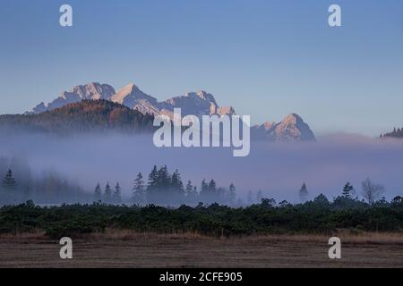 Clouds of fog on the Barmsee against Wetterstein Mountains with Alpspitze, Zugspitze and Waxenstones, autumn, trees, blue sky, Krün, Stock Photo