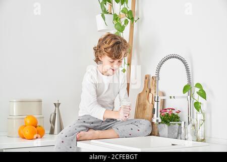 Blond child washing his hands in the kitchen sink to prevent any infection Stock Photo