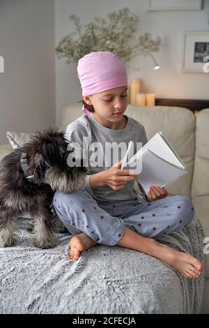 From below happy little child with cancer disease writing notes while sitting with dog on bed in room Stock Photo