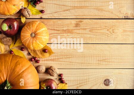Autumn holiday concept with pumpkins, fallen leaves, nuts, red berries on wooden table. Thanksgiving background. Flat lay, top view, copy space. Stock Photo