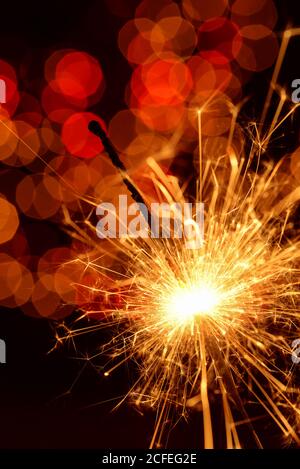 Burning sparkler against golden bokeh on black background Stock Photo