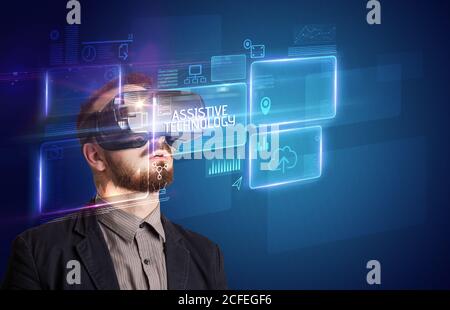 Businessman looking through Virtual Reality glasses with ASSISTIVE TECHNOLOGY inscription, new technology concept Stock Photo