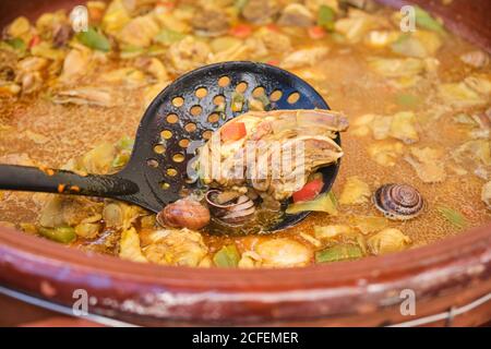 Skimmer in large clay pot with cooking dish of chicken rice assorted vegetables and snails Stock Photo