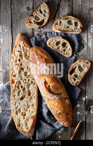 From above whole and halved appetizing baguettes arranged on white towel against rustic wooden background Stock Photo