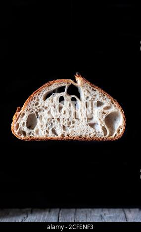 Pieces of tasty fresh bread falling on napkin on table against black background Stock Photo
