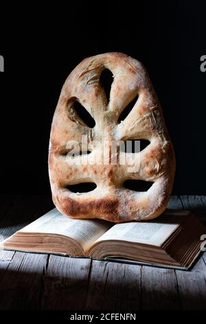 Loaf of fresh fougasse bread placed on open recipe book on wooden table against black background Stock Photo