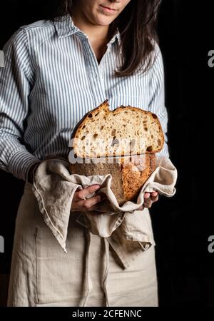 Crop Woman baker in apron holding cut in half loaf of fresh healthy artisan bread Stock Photo
