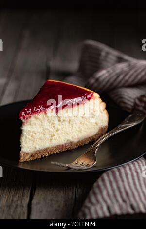 Delicious homemade cheesecake with red berry jam served on black plate on wooden table Stock Photo