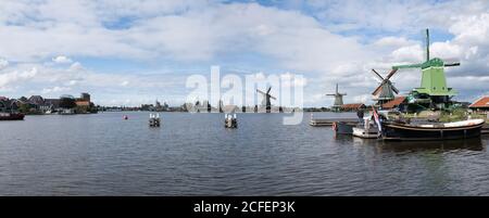 Panoramic view of six windmills in a row at the river Zaan in the Zaanse Schans, the Netherlands. Blue cloudy sky Stock Photo