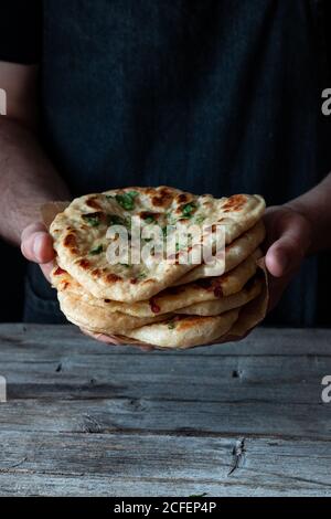 unrecognizable man holding stack of fresh naan flatbread over lumber table in rustic kitchen Stock Photo
