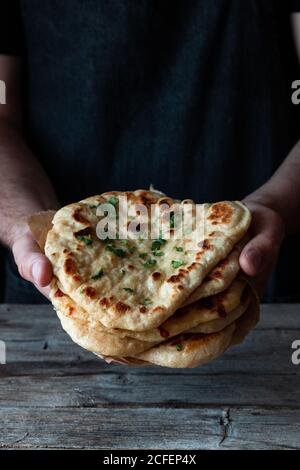 unrecognizable man holding stack of fresh naan flatbread over lumber table in rustic kitchen Stock Photo