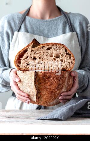 Hands of Woman in kitchen apron holding both hands cutting homemade bread Stock Photo
