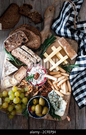 From above composition of fresh rye bread, cheese, grape bunch and olives placed on wooden board Stock Photo