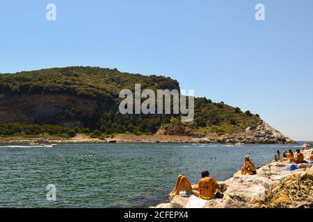 Vacationers sunbathing on the rocky shore of Porto Venere in front of the Palmaria Island in a sunny summer day, La Spezia, Liguria, Italy Stock Photo
