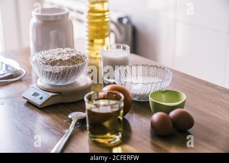 Ingredients for preparing homemade aromatic orange muffins placed on wooden counter near window in modern kitchen Stock Photo
