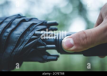 Closeup crop man hand with handle of umbrella pressing button for open umbrella on blurred background Stock Photo