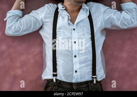 Top view crop unrecognizable man in white shirt and suspenders lying down floating in pink sea at sandbank