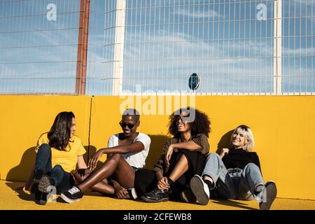 Carefree youthful diverse women in casual clothes laughing and having friendly conversation while sitting in sport playground Stock Photo