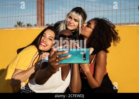 Carefree youthful multiracial women in casual clothes enjoying freedom and taking selfie on cellphone while spending time on stadium Stock Photo