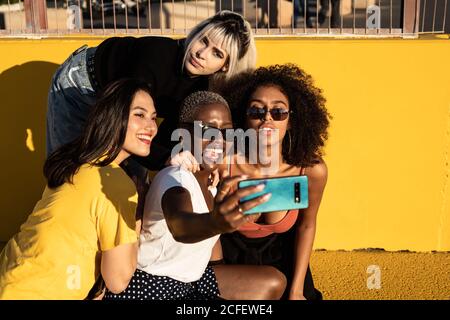 Cheerful young diverse female friends taking selfie on smartphone in street Stock Photo