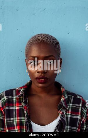 Young African American female with short hair and piercing wearing black plaid shirt looking at camera with intense eyes and challenge while feeling sad