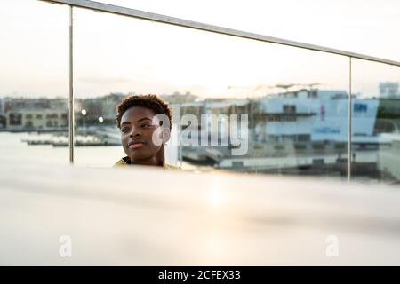 Selective focus side view of serene African American Woman chilling on glass balcony and looking away Stock Photo