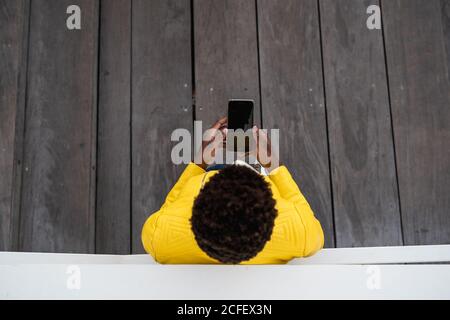 Top view of unrecognizable black Woman leaning on wall while using mobile phone Stock Photo