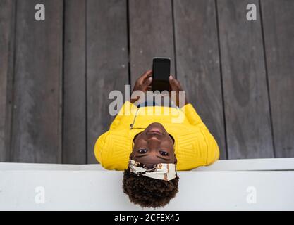 Top view of modern African American Woman leaning on wall of modern building while using mobile phone Stock Photo