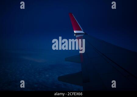 Through window view of wing of modern airplane flying over clouds in dark night time Stock Photo