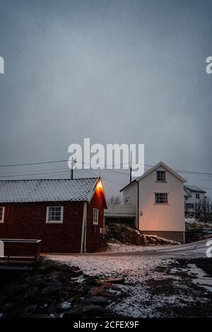 Dark red striped cottage with white windows and snowy roof in small town in overcast weather in Lofoten Stock Photo