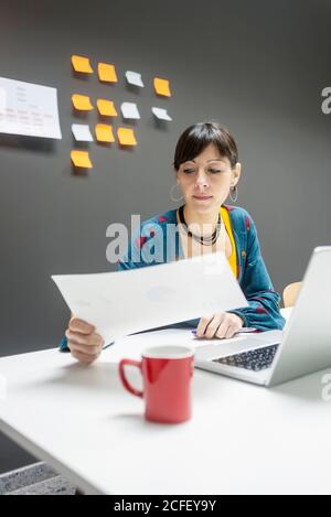 Pretty female working with documents while sitting at desk in modern office Stock Photo