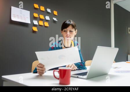 Pretty female working with documents while sitting at desk in modern office Stock Photo