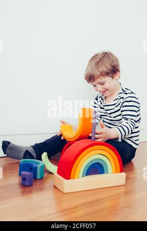 Blonde cute boy playing with waldorf rainbow puzzle Stock Photo