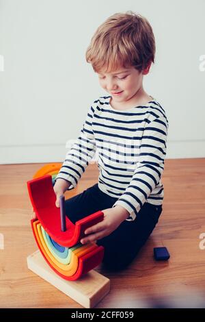 Blonde cute boy playing with waldorf rainbow puzzle Stock Photo