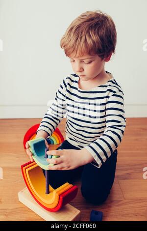 Blonde cute boy playing with waldorf rainbow puzzle Stock Photo