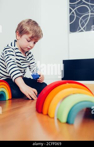 Blonde cute boy playing with waldorf rainbow puzzle Stock Photo