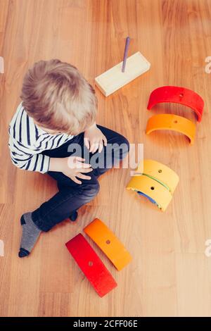 Blonde cute boy playing with waldorf rainbow puzzle Stock Photo