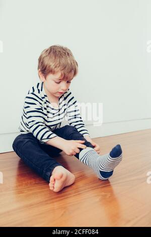 Funny kid wearing socks and sitting on floor in room Stock Photo
