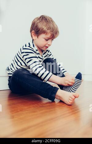 Funny kid wearing socks and sitting on floor in room Stock Photo