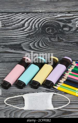 Colored pencils and colored markers. Nearby is a medical mask. On brushed pine boards painted black and white. Stock Photo