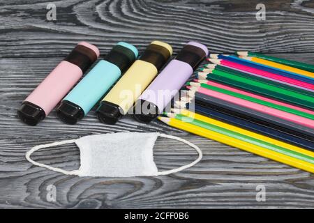 Colored pencils and colored markers. Nearby is a medical mask. On brushed pine boards painted black and white. Stock Photo