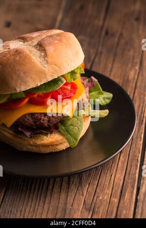 Homemade deluxe burger with cheese, lettuce, tomato and pickles on dark moody background Stock Photo