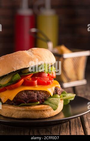 Homemade deluxe burger with cheese, lettuce, tomato and pickles on dark moody background Stock Photo