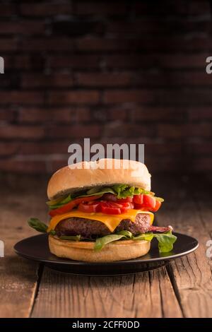 Homemade deluxe burger with cheese, lettuce, tomato and pickles on dark moody background Stock Photo